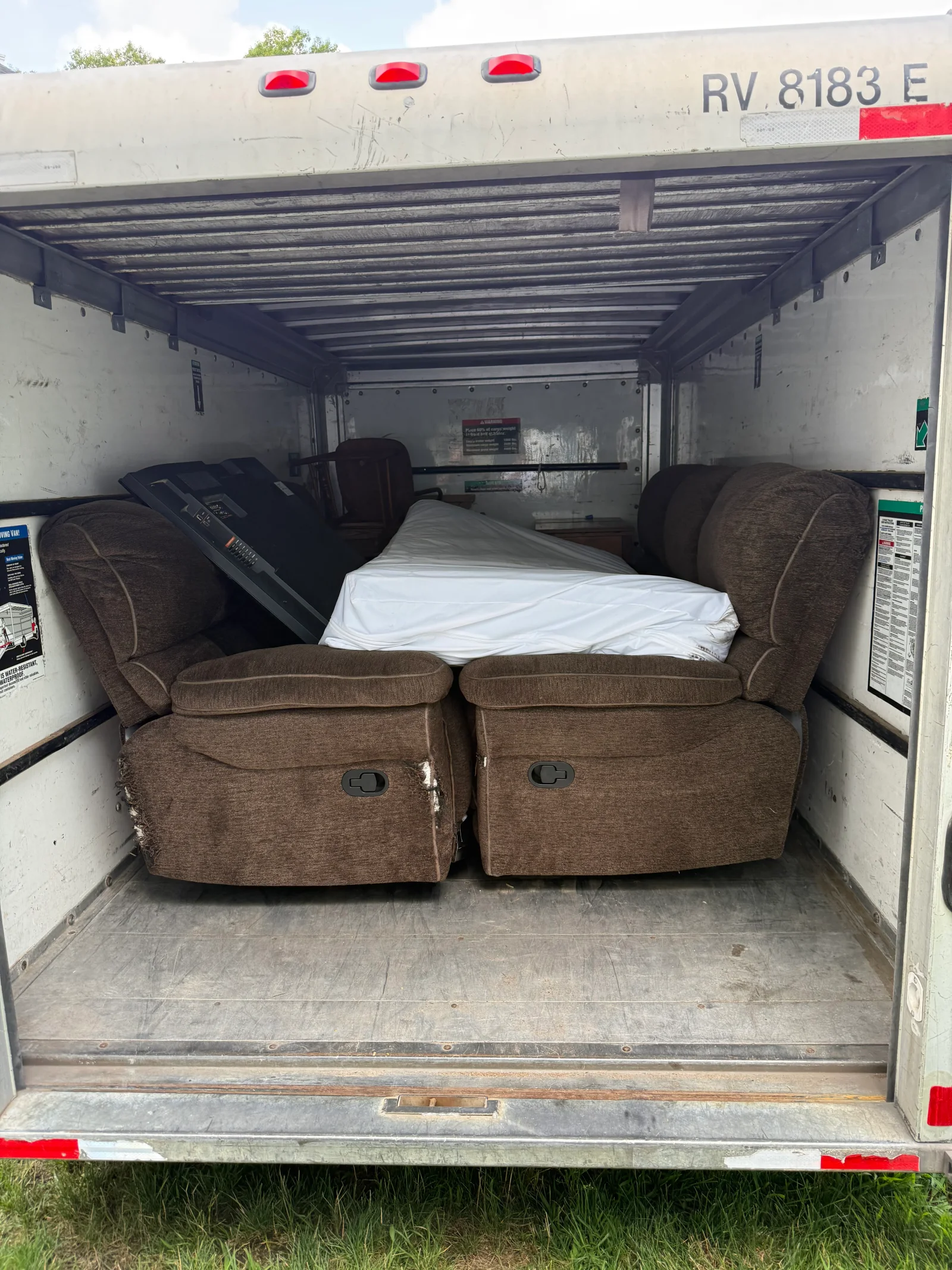 Brown chenille recliners, a wrapped white mattress, and a folded metal frame loaded in a cargo truck