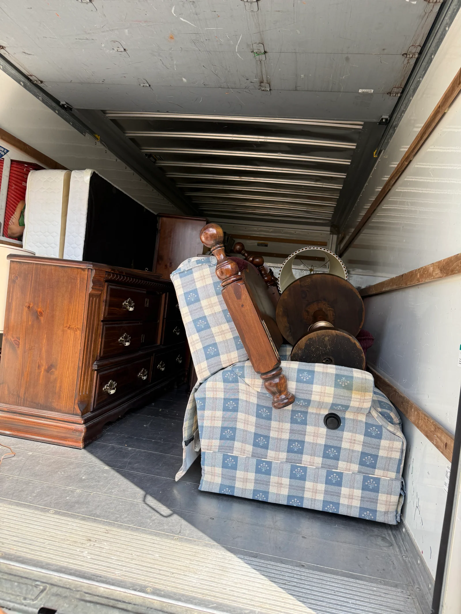Dresser, plaid recliner, mattresses, and wood headboard loaded in a box truck for junk removal