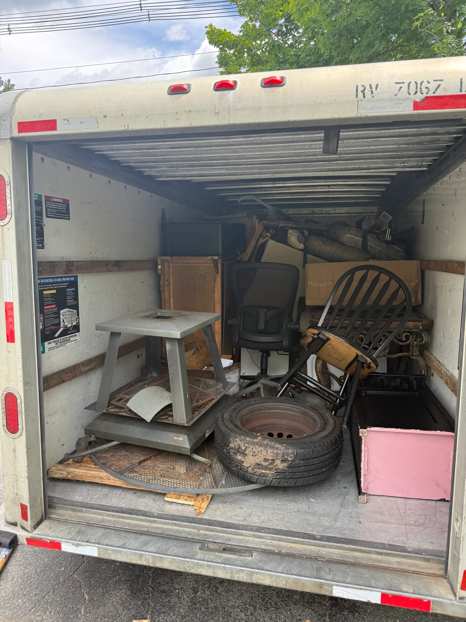 Box truck interior filled with discarded furniture, office chair, metal table, tire, and cardboard boxes for junk removal