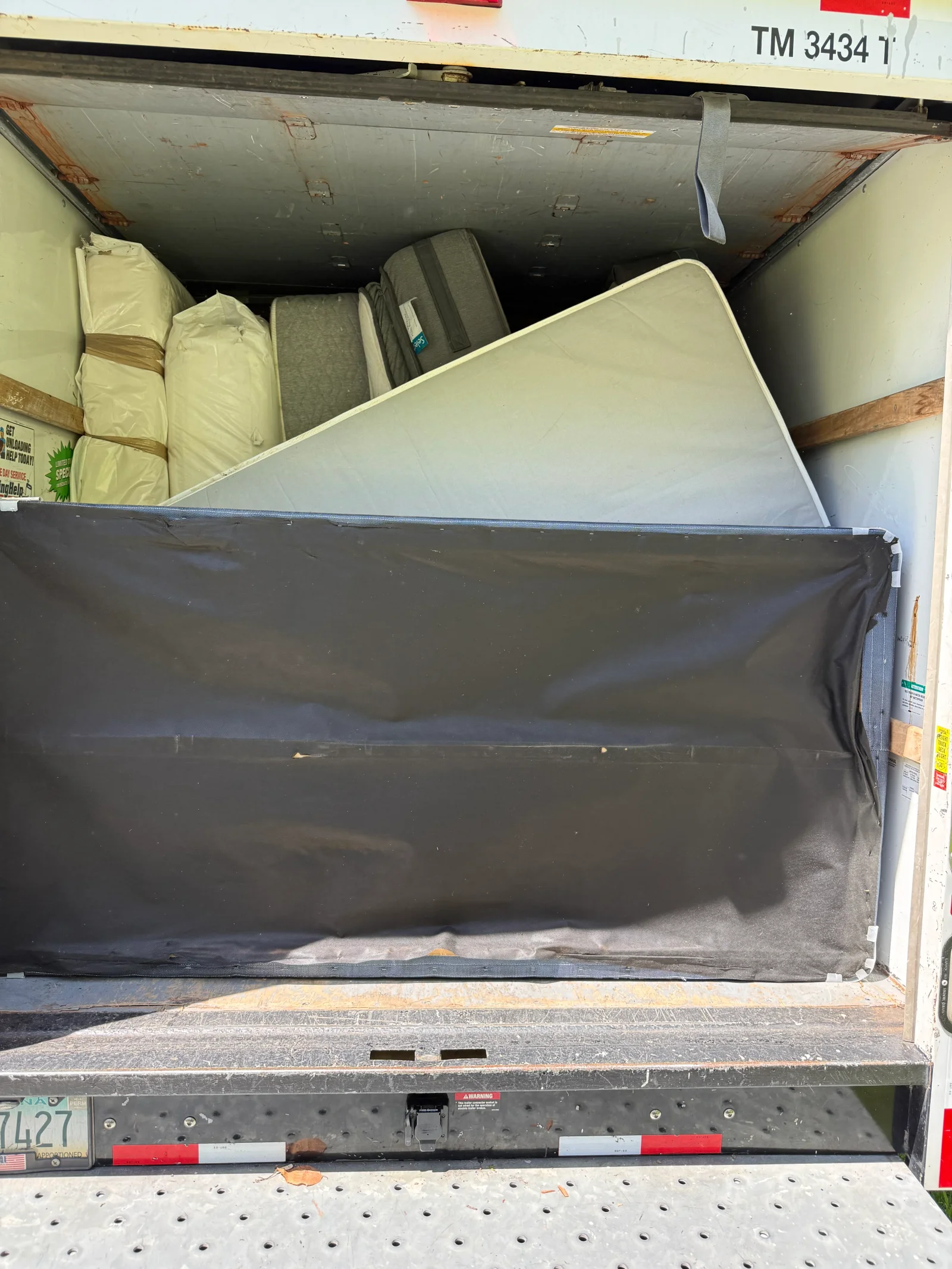 Box truck loaded with wrapped and tarp-covered mattresses secured with straps and wood blocking