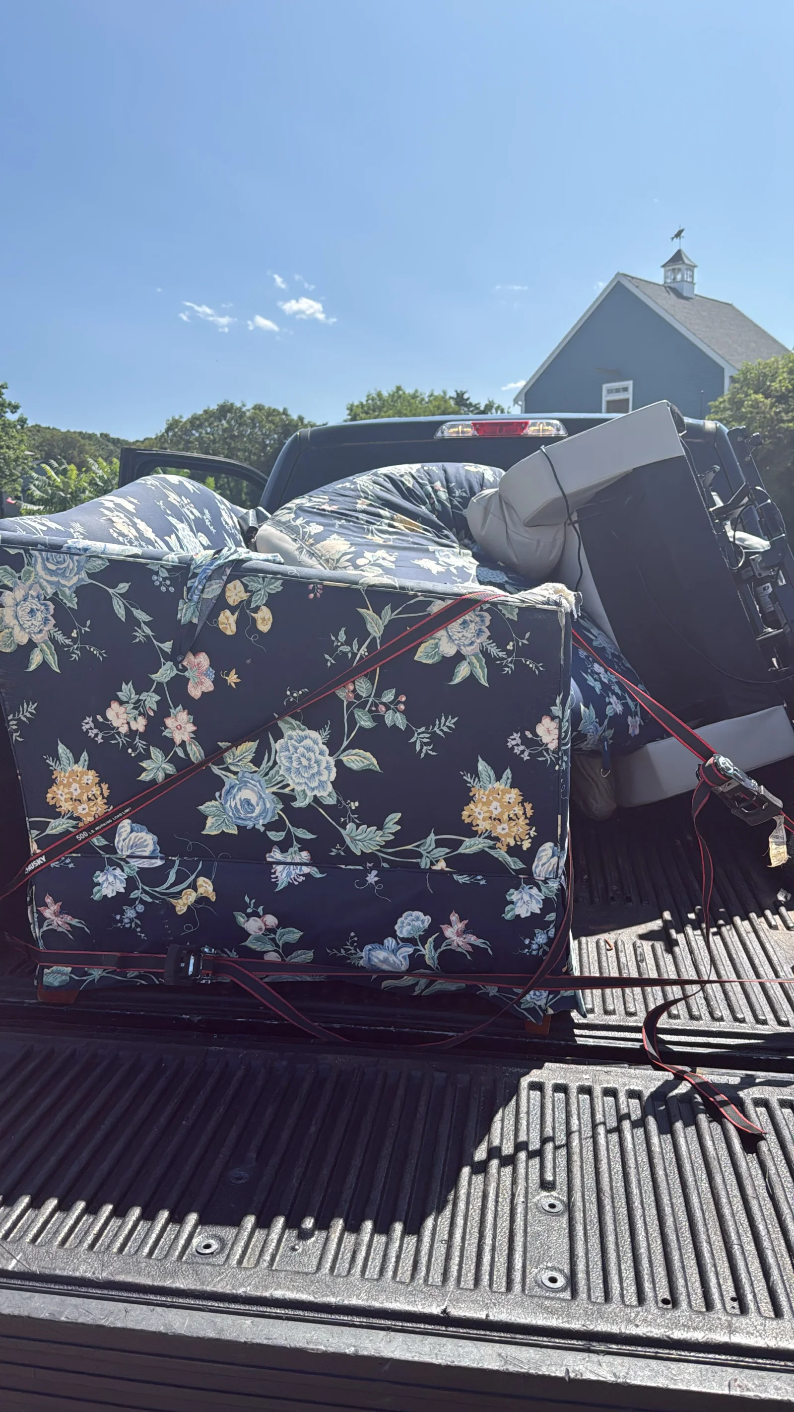 Navy floral sofa and gray cushion strapped with red ratchet straps in a pickup truck bed