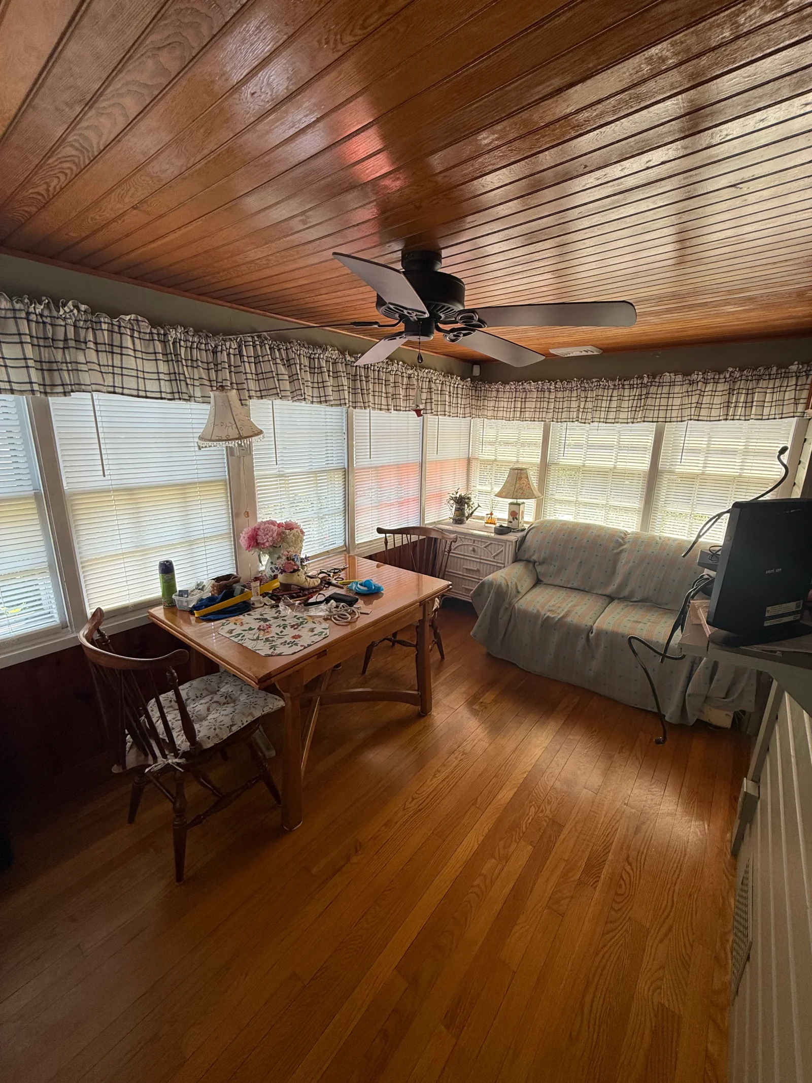 Sunroom with wood plank ceiling, hardwood floors, slipcovered sofa, wooden dining table and chairs, and white horizontal blinds