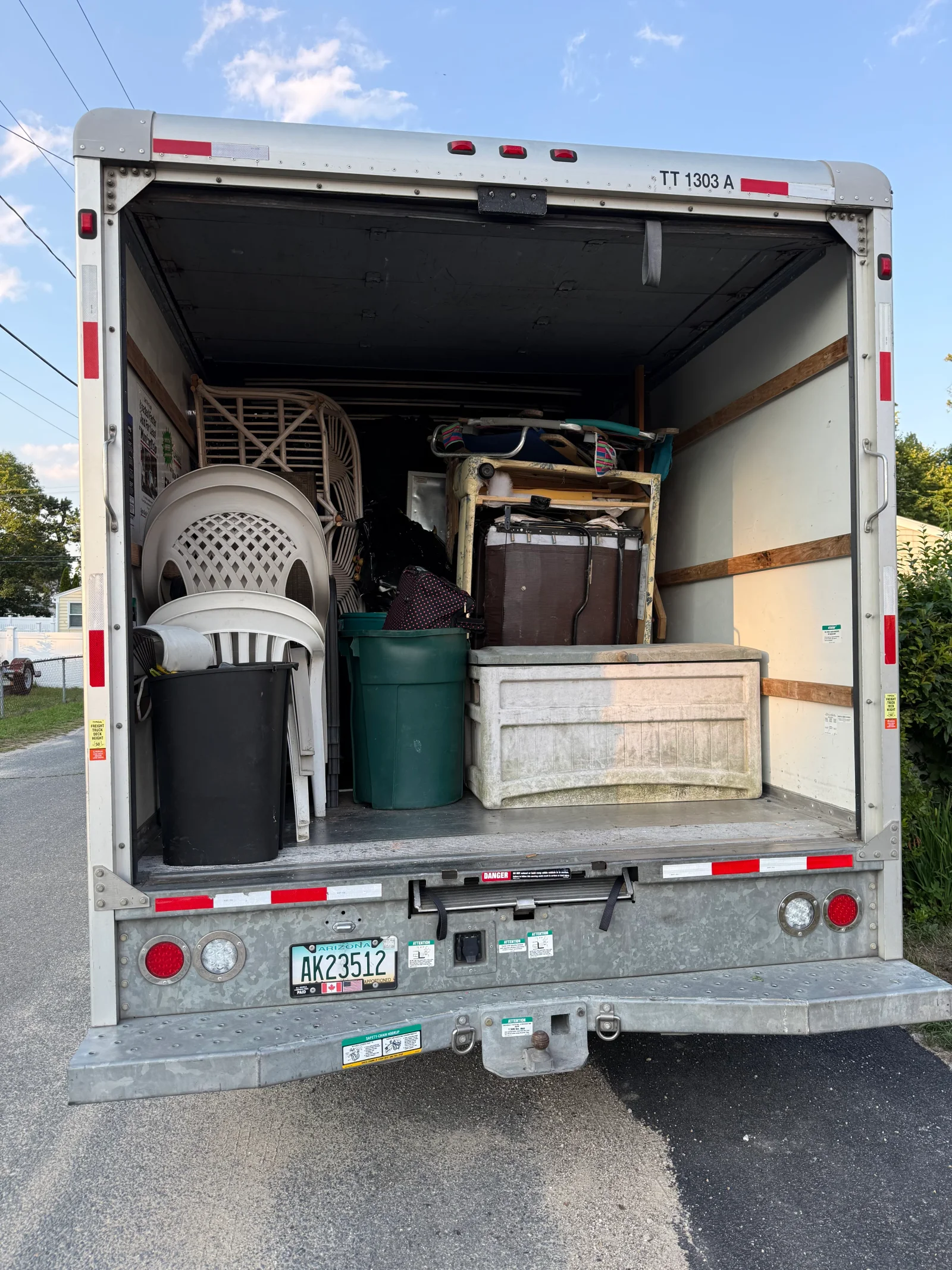 Box truck cargo area loaded with stacked plastic chairs, wicker furniture, storage bin, and trash cans for junk removal