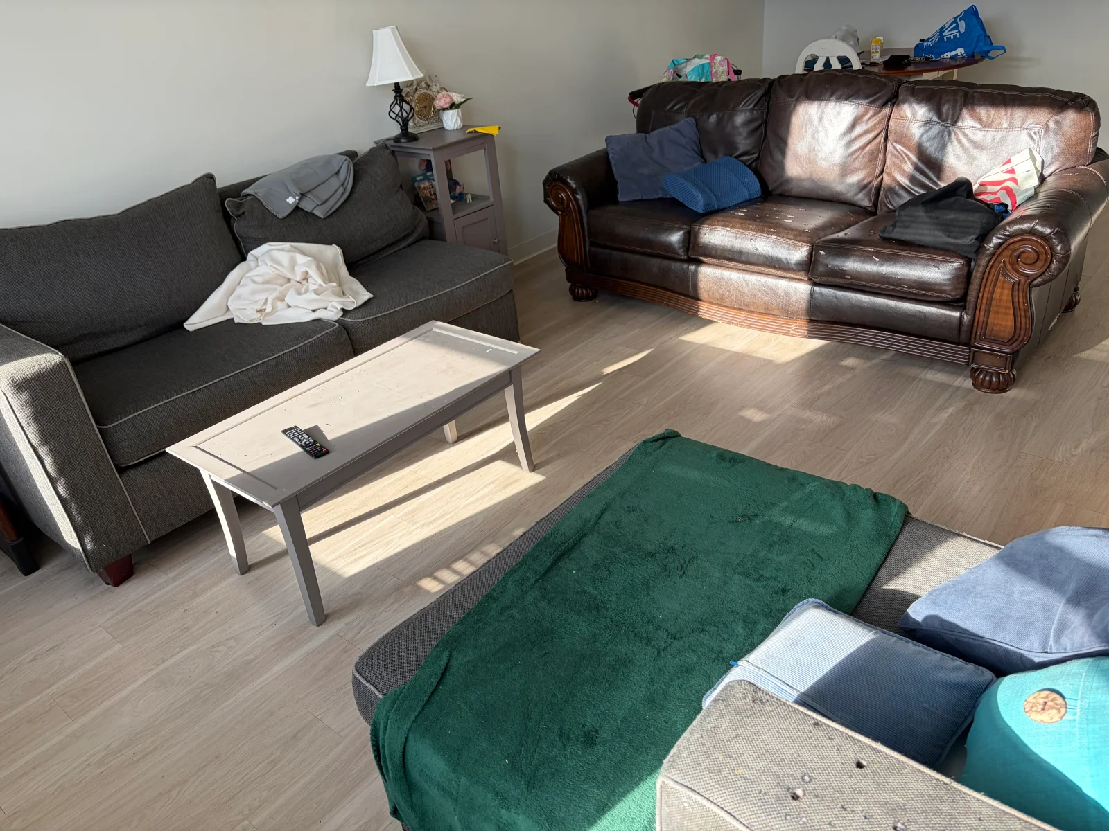 Brown leather loveseat, gray fabric sofa, and coffee table on wood-look vinyl plank flooring before furniture removal