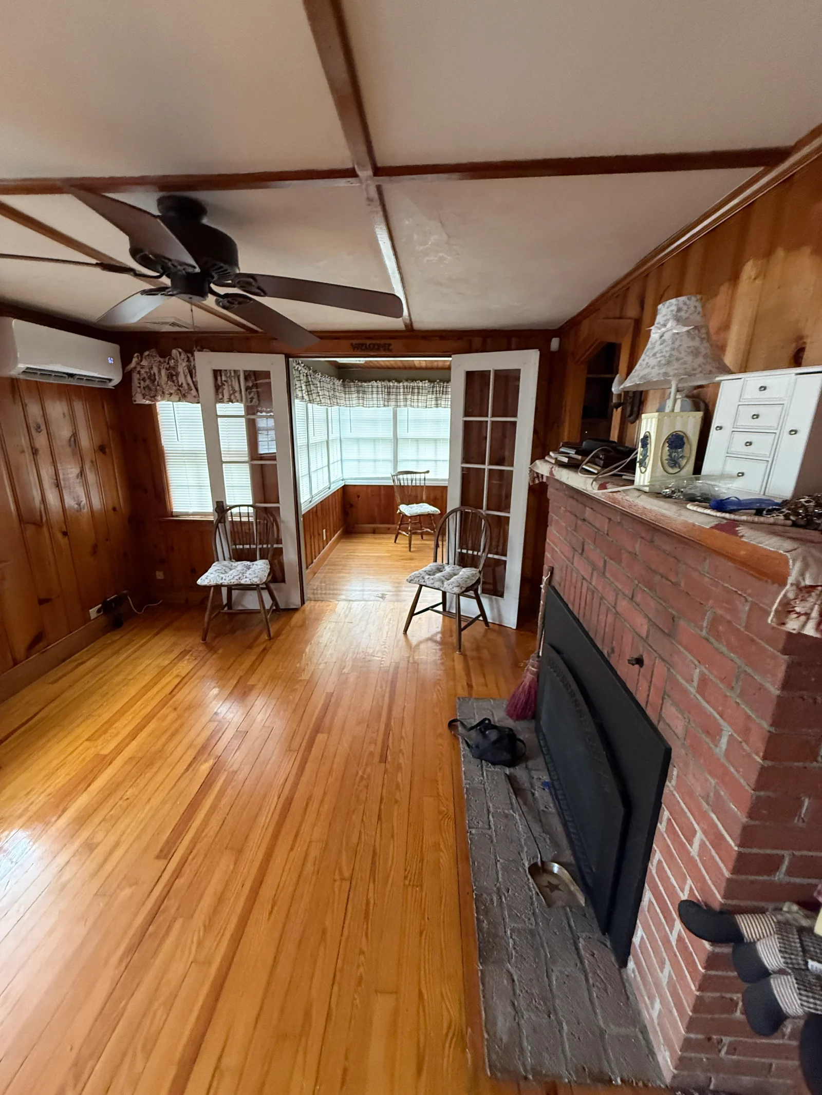 Knotty pine paneled living room with hardwood floors, brick fireplace, and French doors to sunroom