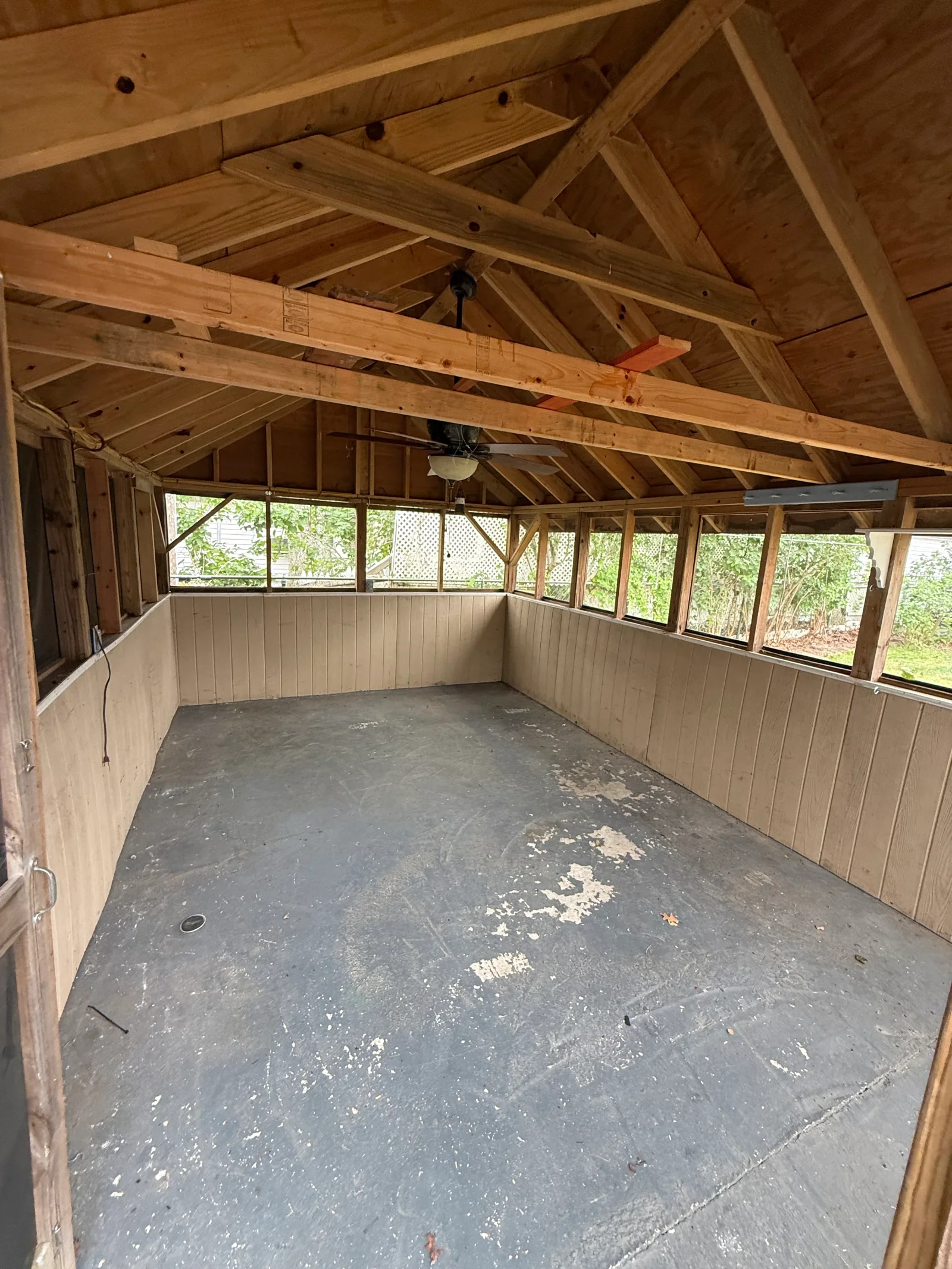 Interior of wood gazebo with exposed pine rafters, tan paneled walls, and gray concrete floor with peeling paint